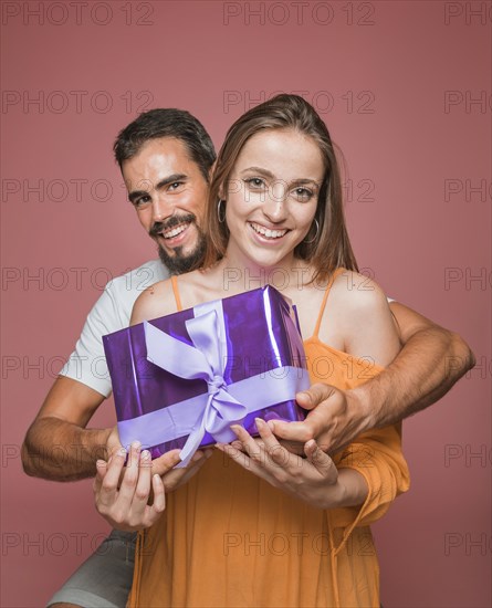 Beautiful couple holding purple gift box against colored background
