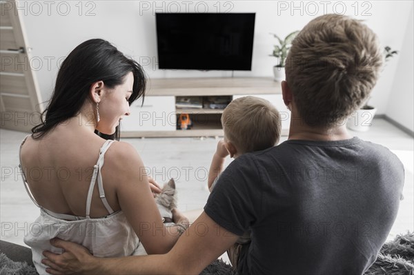 Rear view young couple sitting with their dog baby boy watching television