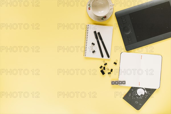 Graphic digital tablet ceramic empty cup with stationeries yellow background