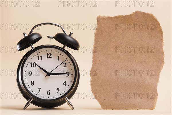 Blank brown torn paper near black alarm clock against colored backdrop