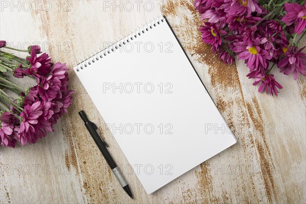 Overhead view spiral notepad with pen pink flowers wooden background