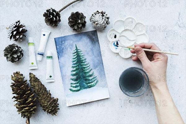 Close up person s hand painting christmas tree with acrylic paint tubes