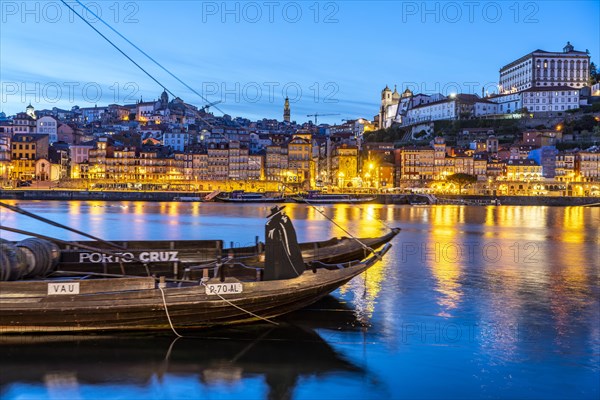 View over the traditional Rabelo boats on the Douro riverbank in Vila Nova de Gaia towards the old town of Porto at dusk