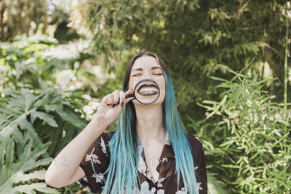 Young woman holding magnifying glass front her mouth