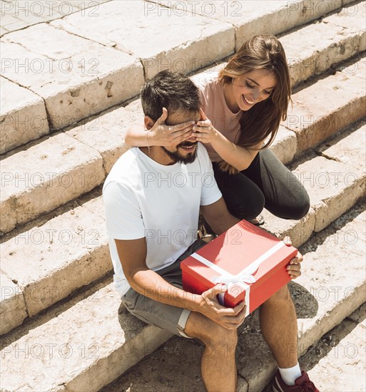 Woman covering her boyfriend s eyes surprising him with gift