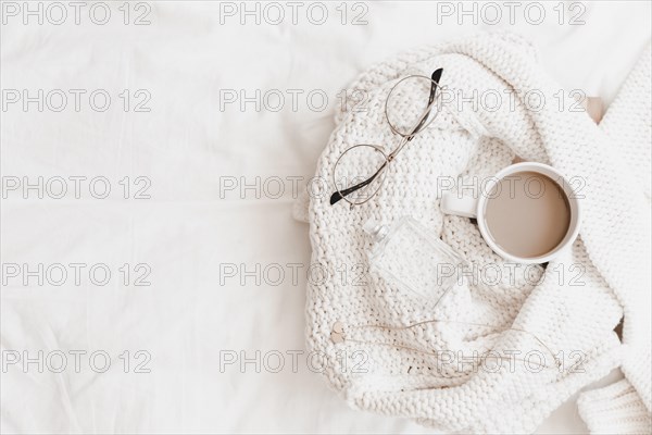 Hot drink necklace eyeglasses perfume sweater placed bedsheet