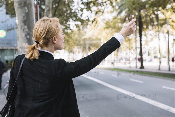 Rear view young woman hailing rideshare taxi car road
