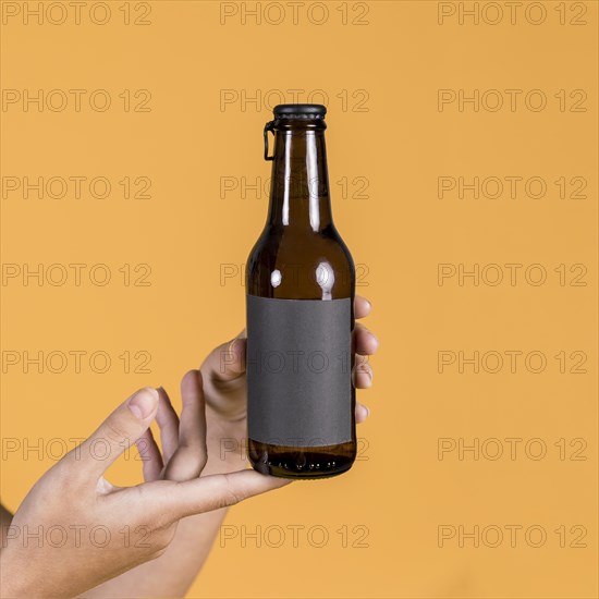 Person s hand holding beer bottle yellow background