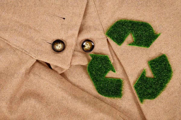 Recycling arrow symbol made out of grass on beige coat. Concept for environmental friendly produced clothing
