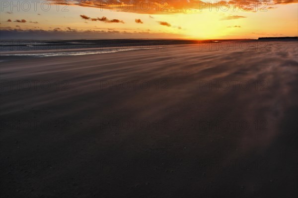 Sand drifting on the beach of the island of Minsener Oog at sunset