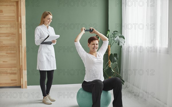 Elder woman covid recovery doing physical exercises with dumbbell while nurse checks