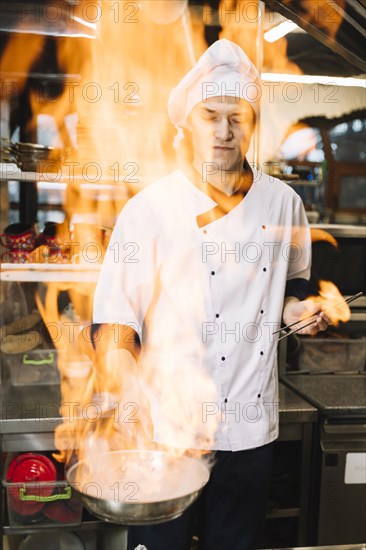 Young cook holding burning pan hand