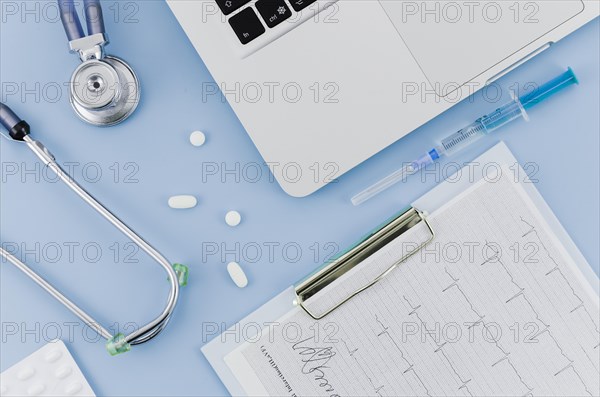 Stethoscope pills syringe laptop ecg medical report clipboard blue backdrop