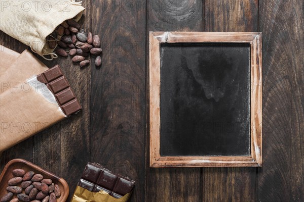 Blank wooden slate with cocoa beans chocolate bars wooden table