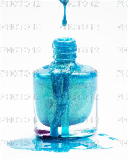 Close up blue glitter nail polish dropping its flask against white background