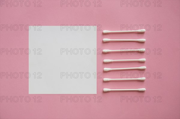 Row cotton swabs near blank adhesive note pink background