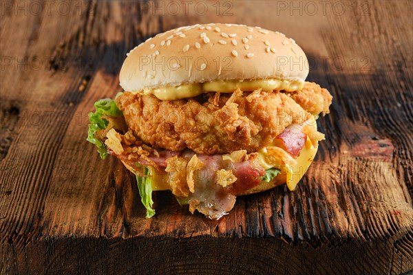 Chicken burger with bacon and cheese on wooden board