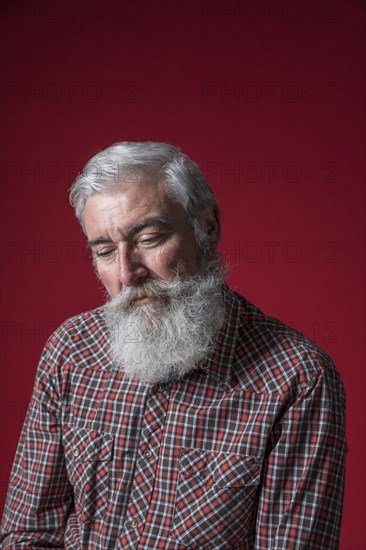 Portrait depressed senior man against red background