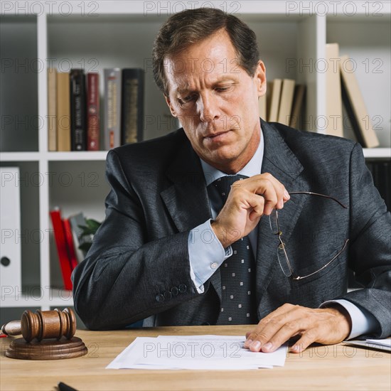 Serious mature lawyer reading document desk courtroom