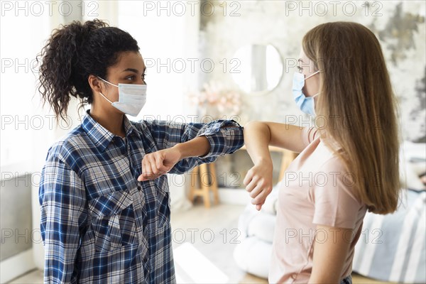 Side view female friends with medical masks practicing elbow salute