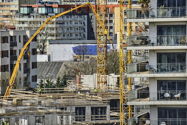 Construction workers install formwork and iron rebars or reinforcing bar for reinforced concrete partitions at the construction site of a large residential building. Pouring concrete from concrete hopper on sunny spring day. Modern cityscape