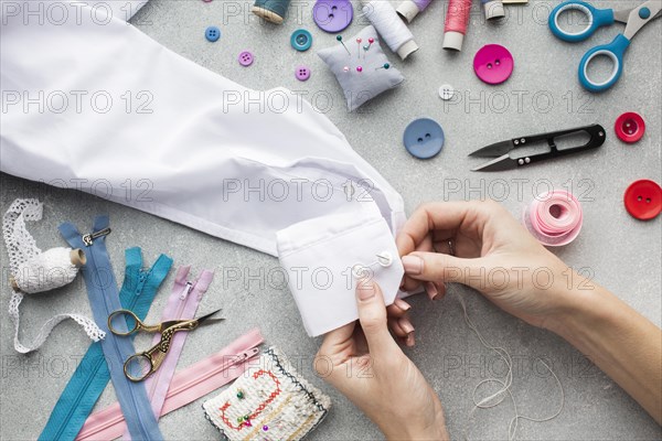 Woman hands sewing white shirt top view