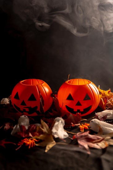 Halloween pumpkins over autumn leaves and ghosts with smoke on a black background