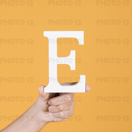 Close up hand holding up uppercase capital letter e yellow background