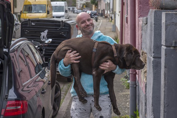 Young man carries his sick dog to the car