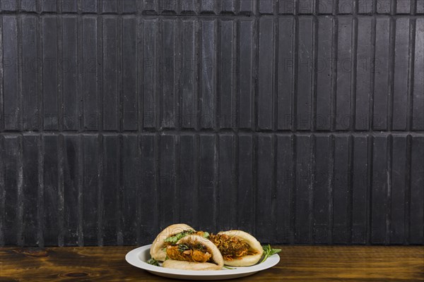 Asian cuisine gua bao steamed buns with vegetable wooden table against black wall