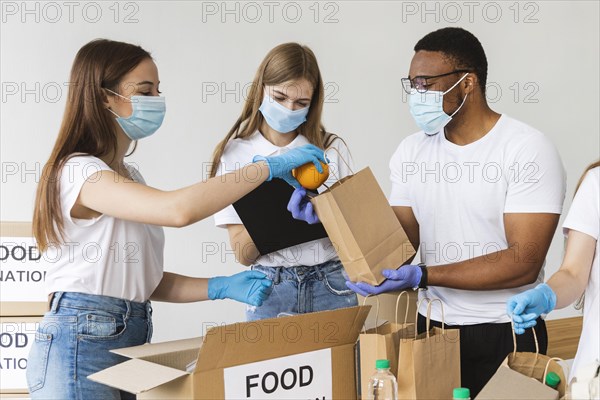 Volunteers with gloves medical masks preparing box with food donation