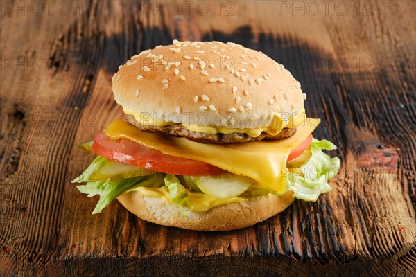 Beef cheeseburger with vegetables and cheesy sauce on wooden board