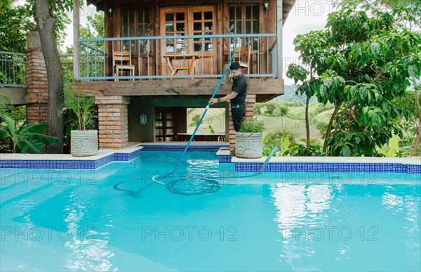 Maintenance man cleaning swimming pool with vacuum suction hose. Worker cleaning a beautiful swimming pool with suction hose