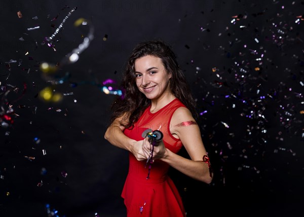 Young smiling woman with popper tossing confetti