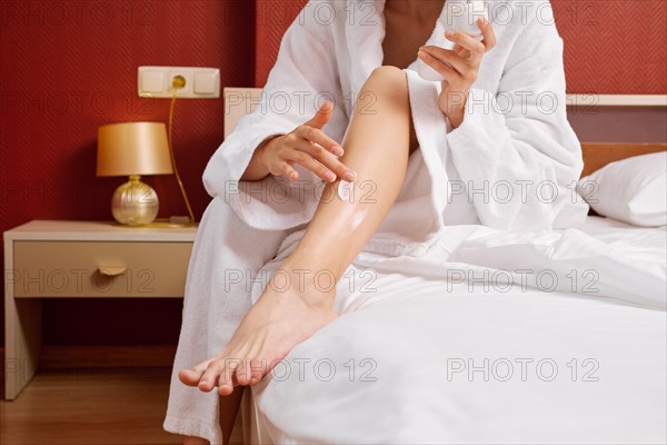 Unrecognizable woman rubs foot cream sitting on the edge of her bed