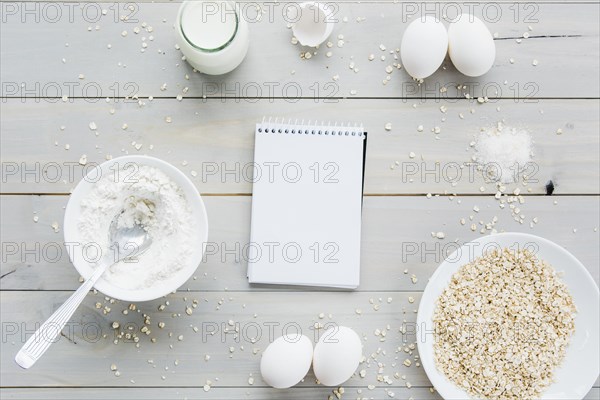 High angle view spiral notepad oats eggs flour milk wooden backdrop