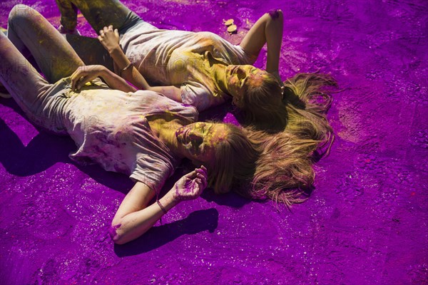 Two young women lying side by side purple holi powder