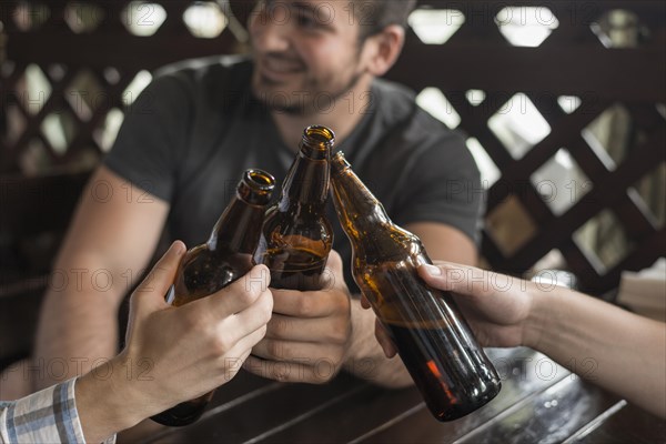 Anonymous friends clinking bottles bar table