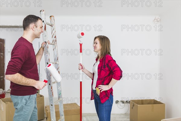 Side view couple with paint rollers ladder