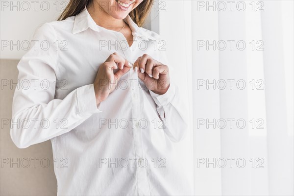 Smiling young woman putting button her white shirt