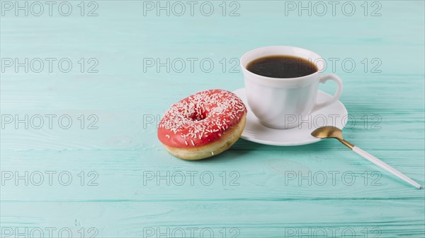 Yummy donut with cup tea spoon green table
