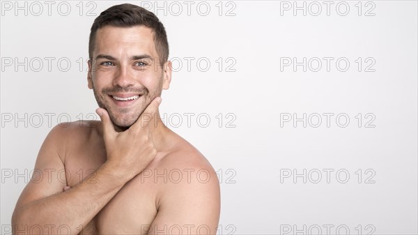 Handsome young smiling man looking camera keeping hand chin while standing against white wall