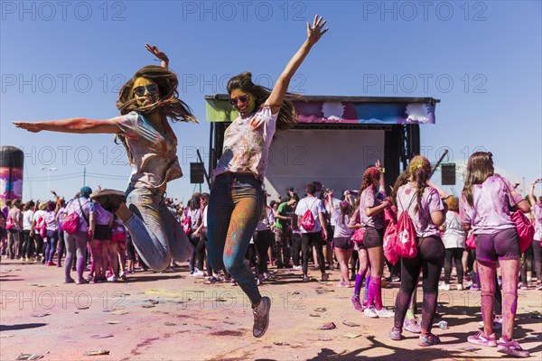 Excited young women jumping air celebrating holi festival