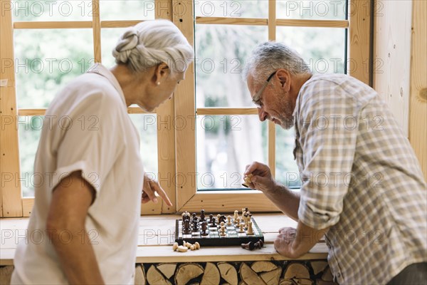 Senior couple playing chess window sill
