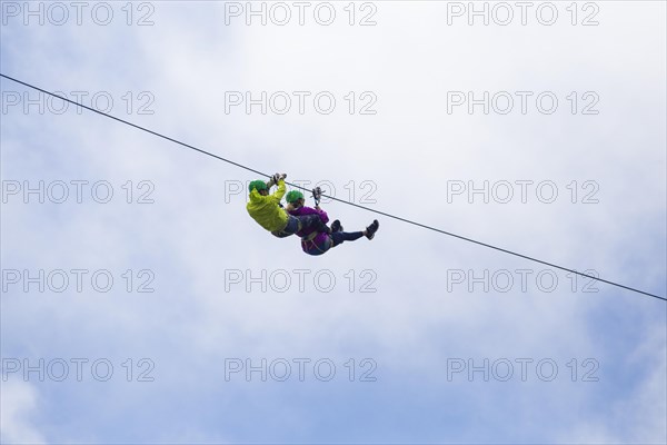 Adventurous tourist zip lining against cloudy sky