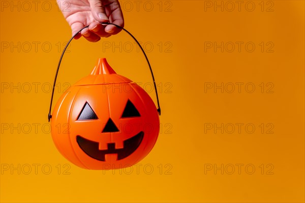 Hand holding an orange Halloween pumpkin on a background of yellow