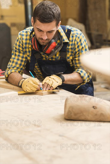 Male carpenter measuring wooden block with ruler pencil