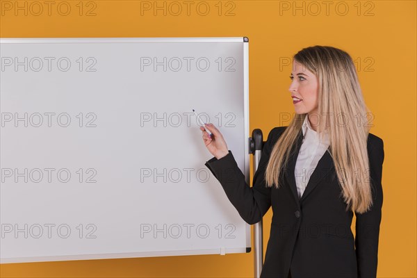 Confident young businesswoman giving presentation whiteboard against orange backdrop