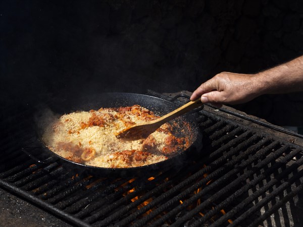 Cook mixing rice with calamari rings vegetables frying pan