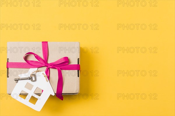 Gift box tied with key house model bright yellow background